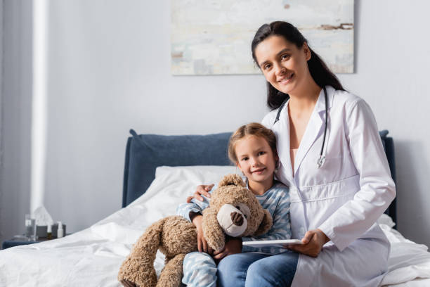istock smiling pediatrician embracing sick girl with teddy bear while looking at camera 1288067841