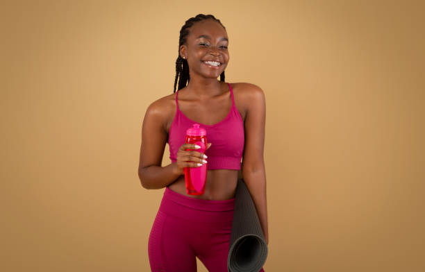 estilo de vida deportivo. mujer negra en ropa deportiva sosteniendo colchoneta fitness y botella de agua - aerobics beautiful bottle body fotografías e imágenes de stock