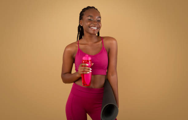 спортивный образ жизни. черная женщина в спортивной одежде холдинг фитнес коврик и бутылка воды - aerobics beautiful bottle body стоковые фото и изображения