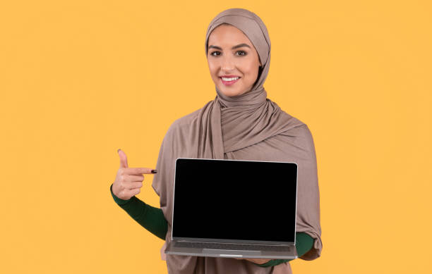 istock Muslim Lady Pointing At Laptop Empty Screen, Yellow Background, Mockup 1288073998
