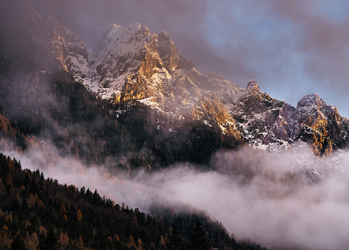 Sun lightening snowcapped mountain range through clouds during winter day in Kranjska gora, Slovenia.