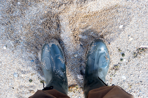 Man in brown pants and rubber boots on the sandy beach, top view.