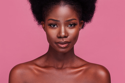 Beautiful portrait of a gorgeous African American fashion model with bare shoulders and afro hair isolated on dirty pink background.