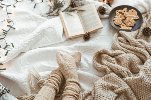 Cozy winter day at home in bed with warm knitted blanket, book and gingerbread cookies Cozy winter day at home with warm knitted blanket, book and gingerbread. Woman wearing warm woolen socks on cold winter weekend. Christmas, relaxation and hygge concept hygge stock pictures, royalty-free photos & images