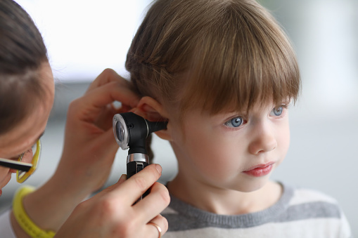 Otorhinolaryngologist examines little girl's ear with otoscope. Adenoiditis as cause of otitis media in children concept.