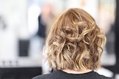 Woman with curly hair sit in beauty salon back view.