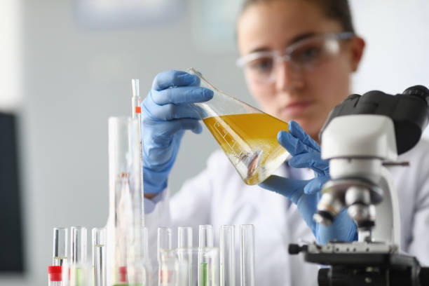 woman chemist holds flask with yellow liquid in her hands in chemical laboratory - laboratory pharmacy medicine research imagens e fotografias de stock