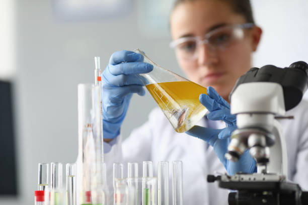 в химической лаборатории женщина-химик держит колбу с желтой жидкостью в руках - laboratory equipment technician laboratory chemist стоковые фото и �изображения