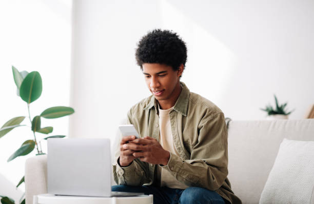 istock Focused black teen guy using laptop and smartphone for online learning at home 1288089682