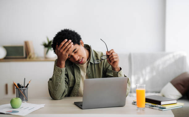 istock Tired black guy suffering from headache during online studies in front of laptop at home, panorama 1288089813