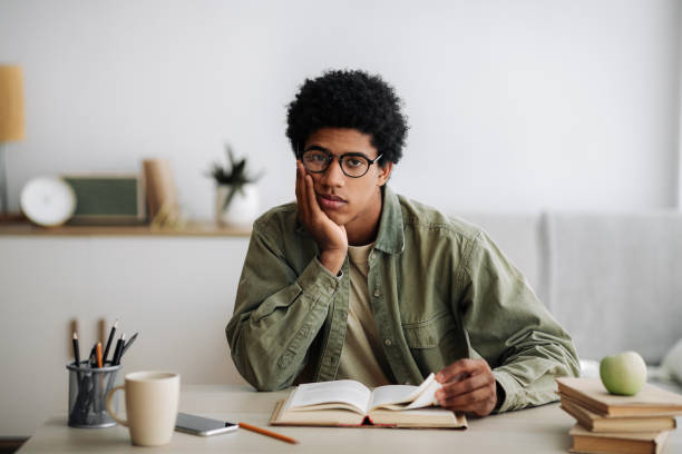 istock Distance education concept. Bored African American student with textbook studying at home 1288089924