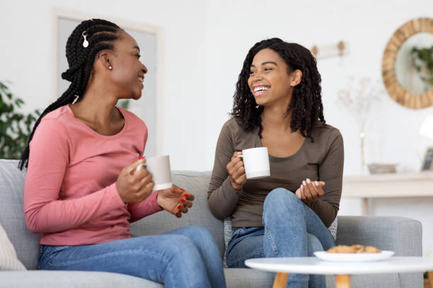 istock African american girlfriends enjoying weekend together, drinking coffee on couch 1288092405