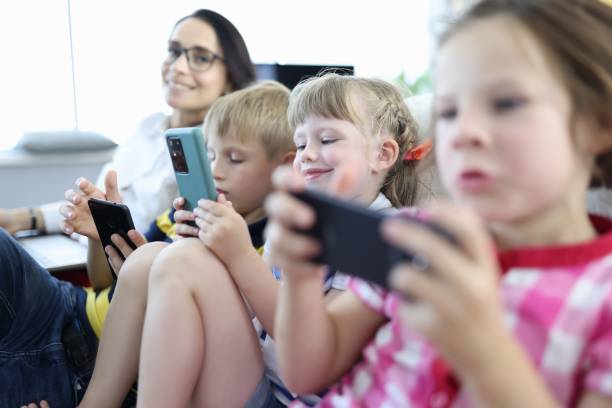 istock Three children sit side by side on couch and play on smartphones. 1288094113