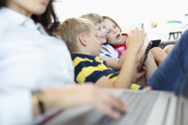 istock Three children sit side by side on couch and play on smartphones. 1288094117