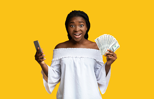 Cashback Concept. Excited Young Woman Holding Smartphone And Dollar Cash