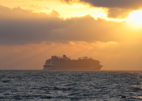 A huge cruise ship moored off the coast due to Covid-19 powers across the horizon as the rising sun bathes the scene in warm golden light.