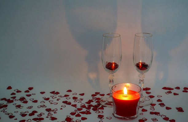 istock Two champagne glasses with a lite candle in front surrounded by heart shaped confetti on a white background 1288101978