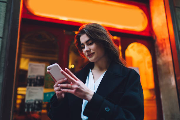 joven turista caucásico disfrutando de viaje en solitario para explorar la ciudad usando la aplicación celular para chatear y mensajes, hermosa chica hipster leyendo recibió correo electrónico en el teléfono inteligente de pie en la urbanidad - urbanity fotografías e imágenes de stock