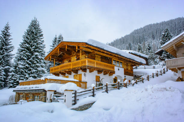 Snow covered street with parked cars and chalets winter holliday homes in a ski resort in the Austrian Alps during a snowy winter day.