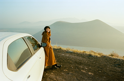 Young Caucasian woman standing near the car and looking at volcano