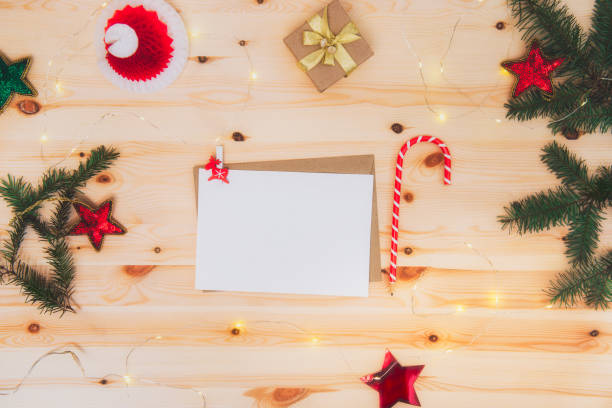 istock Top view empty paper letter wishlist for Santa Claus with envelope, candy shape pencil, gift box and Christmas decor on a wooden table. Festive mood. Flat Lay, selective focus. Copy space. 1288111691