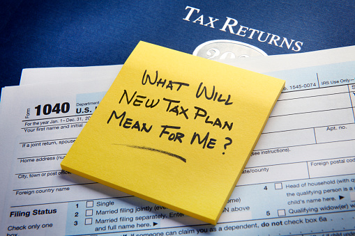 A yellow sticky pad rests on top of a U.S. 1040 income tax return and asks the question as to what the new tax plan would mean for me?