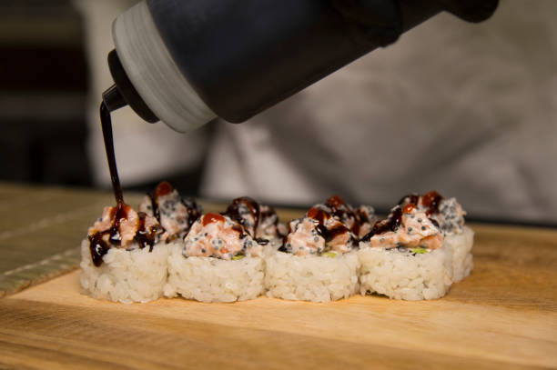 istock Chef preparing sushi. Master serves roll with Unagi sauce from the bottle. Serving process in restaurant kitchen. 1288120462