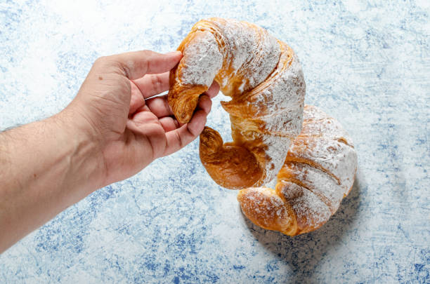 istock Hand holding a freshly baked croissant with icing sugar on a textured blue background 1288122098