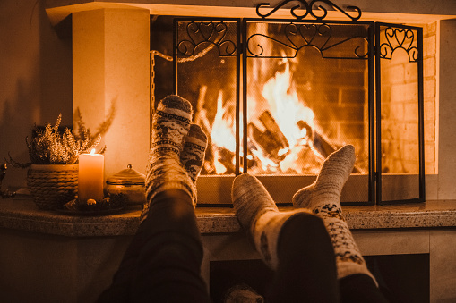 Unrecognizable couple enjoying Christmas Holidays near fireplace at home, they relaxing during covid-19 lockdown.