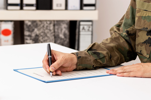 Close up of a hand of a military man writing or signing a document on a desk in the military academy