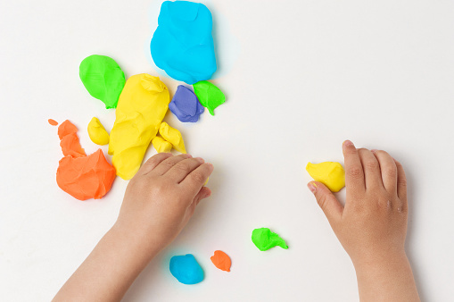 High angle shot of child playing with colorful modeling compound on the table