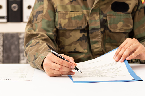 Close up of executive military man hands signing contract on a desk at work