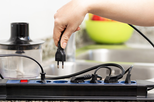 Close up of a woman hand plugging a plug in an electrical socket on a worktop at kitchen