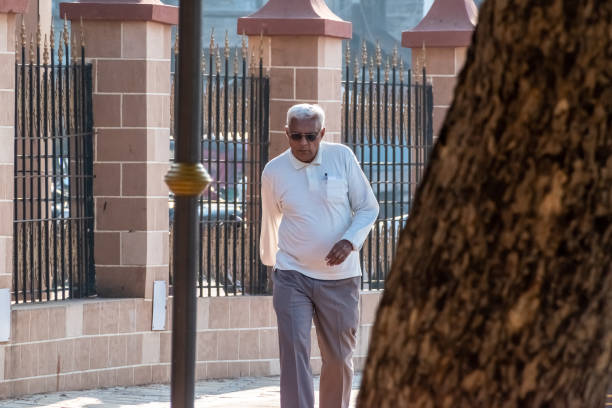 An elderly man taking a walk Jamnagar, Gujarat, India - December 2018: An elderly Indian man wearing sunglasses taking an evening walk in a park. indian man walking in park stock pictures, royalty-free photos & images