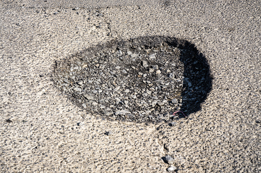 Close-up of a large pothole on the surface of a British street, causing danger for cyclists and drivers.