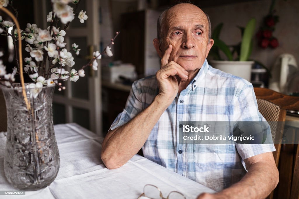 Worried senior man looking in distance Old man sitting at a table with serious face expression Dementia Stock Photo