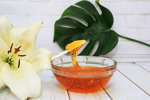 pâte de sucre pour l’épilation dans un bol avec la fleur de lis et la feuille de dracaena dans le vase en verre sur le fond blanc, soin de corps - épilation à la cire photos et images de collection