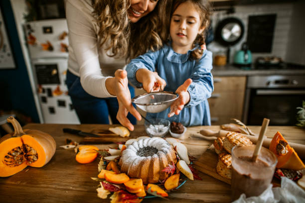 istock Mother and daughter sprinkling icing sugar on cake 1288140584
