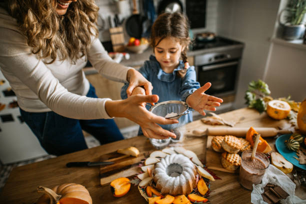 istock Mother and daughter sprinkling icing sugar on cake 1288140723
