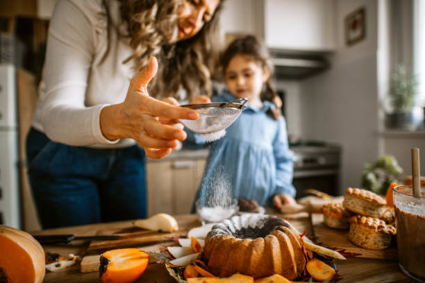 istock Mother and daughter in kitchen dusting cake with powdered sugar 1288140986