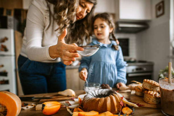 istock Mother and daughter in kitchen dusting cake with powdered sugar 1288141035