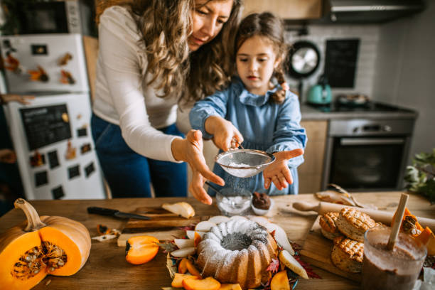 istock Mother and daughter in kitchen dusting cake with powdered sugar 1288141043
