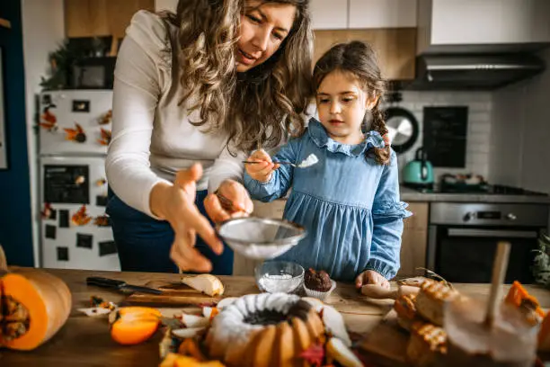 Mother and her little cute daughter are dusting cake with powdered sugar. Having fun together while baking and be creative.