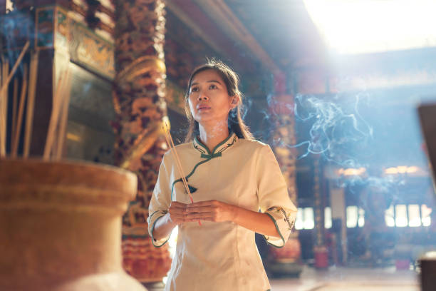 donna asiatica in abiti tradizionali che prega con bastoni joss al tempio buddista - buddhist ceremony foto e immagini stock