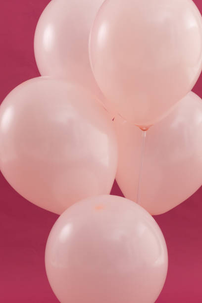 istock Bunch of five pale pink balloons floating on dark red background 1288143367