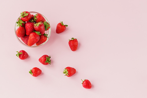 Fresh strawberries in transparent glass bowl top view. Healthy food on light pink table mockup. Delicious, sweet, juicy and ripe berry background