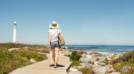Rear view of a young woman walking along a boardwalk by the ocean on a sunny afternoon in summer