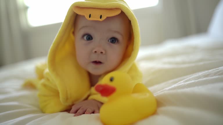 Baby wearing yellow bathrobe duck on parents bed after bath