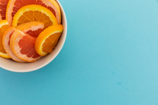 High angle view of bowl of freshly cut orange slices on blue background. fresh healthy fruit copy space concept.