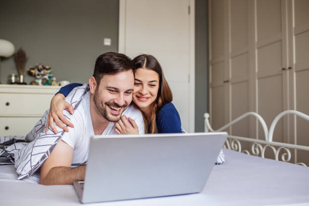 istock Happy couple using laptop at home in bed 1288155846